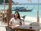 Happy Asian woman in casual white dress sit and relax in seaside outdoor cozy cafÃ© on the beach