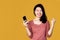 Happy Asian woman get good news hand holding smart phone over yellow background