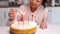 Happy Asian woman lights candles on a birthday cake. Selective focus on cake and face.