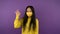 Happy Asian woman in a protective medical mask and dressed in a bright yellow sweater shows OK gesture. isolated purple