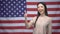 Happy Asian woman showing thumbs-up and winking against USA flag background