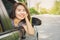 Happy Asian woman sitting in a car smiling to a camera, road trip during vacation, rental car concept