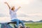 Happy Asian woman spread arms on car roof under sunset at seaside with nature  background during travel in holiday. Confidence