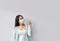 Happy Asian woman in surgical mask pointing finger up at copy space while standing  over white background