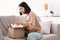 Happy asian woman unpacking parcel sitting on couch