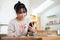 A happy Asian woman is using her smartphone while sitting in a cosy coffee shop