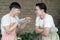 Happy Asian young LGBT gay couple making pizza together. Handsome man showing sliced homemade pizza to his boyfriend for smell