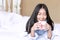 Happy Asian young woman lying holding a cup of coffee on white bed in the morning at home