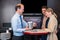 Happy Assistant Showing Compact Speaker To Couple In Shop