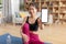 Happy athletic korean lady in sportswear sitting on yoga mat at home and showing modern cellphone with empty screen