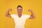 Happy athletic man listen to music in headphones flexing strong arms yellow background, strength