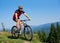 Happy athletic tourist cyclist in helmet, sunglasses and full equipment riding bike on grassy hill