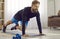 Happy athletic young man doing plank with knee tucks during fitness workout at home