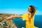 Happy atractive taned woman posing with hand reaching out on cliff edge with beautiful sea view.