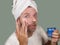 Happy and attractive camp gay man applying moisturizer facial cream with head wrapped in towel feeling confident challenging