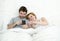 Happy attractive couple in bed using mobile phone smiling watching together internet app