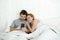 Happy attractive couple in bed using mobile phone smiling watching together internet app