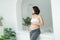Happy Attractive pregnant woman standing near the window and holding her belly. Concepts of pregnancy and family