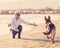 Happy attractive senior woman with her german shepard dog playing on the beach at autumn sunset