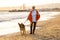 Happy attractive senior woman with her german shepard dog walking on the beach at autumn sunset