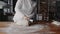 Happy attractive young woman baker wearing uniform cutting dough at kitchen