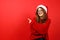 Happy attractive young woman in santa hat and red sweater pointing with finger at empty space for bargain offer