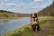 Happy Aussie is resting in park in clearing on warm sunny day. Brown Australian Shepherd puppy sits in green grass by river