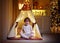 Happy baby boy playing in illuminated teepee tent at home on Christmas holidays