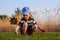 Happy baby boy sitting in grass on the fieald at sunny summer evening. Child outdoors with wind wheel on the river bank