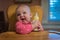 Happy baby girl in high chair grabbing bottle and laughing