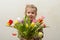 Happy baby girl rejoices and smiles with a bouquet of multi-colored tulips in hands