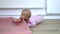 Happy baby lying on the wooden floor and biting a pink mat