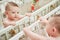 Happy baby is playing with her reflection in the mirror while standing in the crib. Funny child pulls his hand to the mirror, six