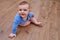 Happy baby toddler crawls on a wooden laminate. Funny child is sitting smiling on the parquet in the home living room, aged 6-11