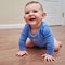 Happy baby toddler crawls on a wooden laminate. Funny child is sitting smiling on the parquet in the home living room, aged 6-11