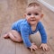 Happy baby toddler crawls on a wooden laminate. Funny child is sitting smiling on the parquet in the home living room, aged 6-11