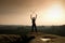 Happy backpacker with x crossed poles in the air, open misty mountain valley bellow cliff. Silhouette of tourist