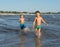 Happy barefoot family having fun - mother, son, together run with splashes by water pool along surf of sunset sea beach. Active