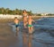 Happy barefoot family having fun - mother, son, together run with splashes by water pool along surf of sunset sea beach. Active