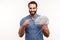 Happy bearded businessman in blue shirt pointing finger at dollar cash in his hand, looking at camera with toothy smile, good