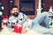 Happy bearded man resting near fireplace at Christmas. Man in knitted sweater sitting in front of the chimney. Guy holds christmas