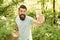 happy bearded man in summer clothes showing water bottle in forest, selective focus, water balance.