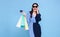 Happy beautiful Asian shopaholic women wearing blue dress and credit card holding shopping bags isolated on blue background