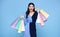 Happy beautiful Asian shopaholic women wearing blue dress and holding shopping bags isolated on blue background
