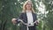 Happy beautiful Caucasian businesswoman in eyeglasses standing in summer park holding bicycle steering wheel. Portrait