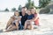 Happy beautiful Caucasian family having holidays on the beach smiling with mother and father sitting on sand with little son and y