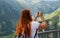 Happy beautiful ginger woman with camera. Hipster fashion gloger girl stands on the background of mountain peaks. Travel concept