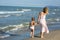 Happy beautiful mom and child walk far away along the sea beach, wind blowing