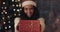 Happy Beautiful Mulatto Girl in Santas Hat Offering and Taking back Gift Box, Looking to Camera and Smiling Standing at