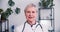 Happy beautiful senior Caucasian female doctor wearing lab coat and stethoscope smiles at camera sitting at light office